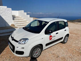 A white rental car parked outside a Greek villa